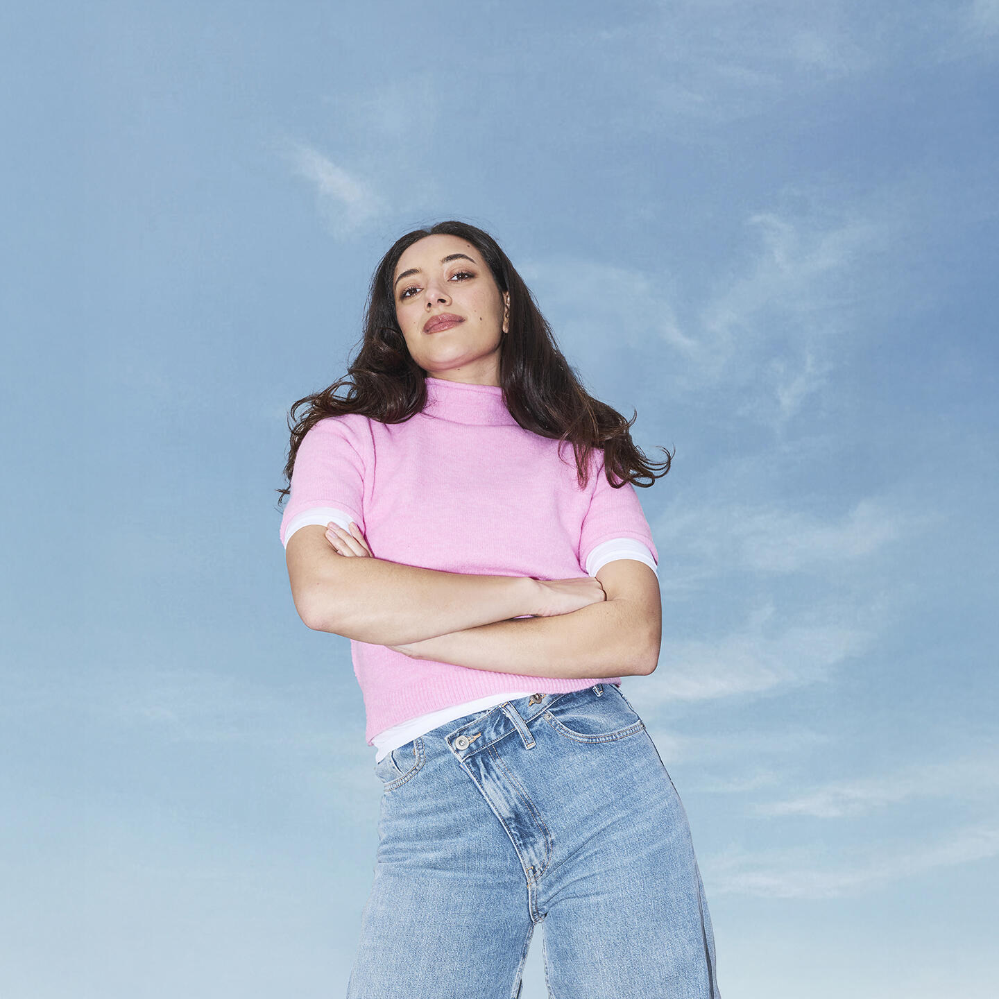 Vrouw met bruin haar en roze top vanuit low angle met armen over elkaar